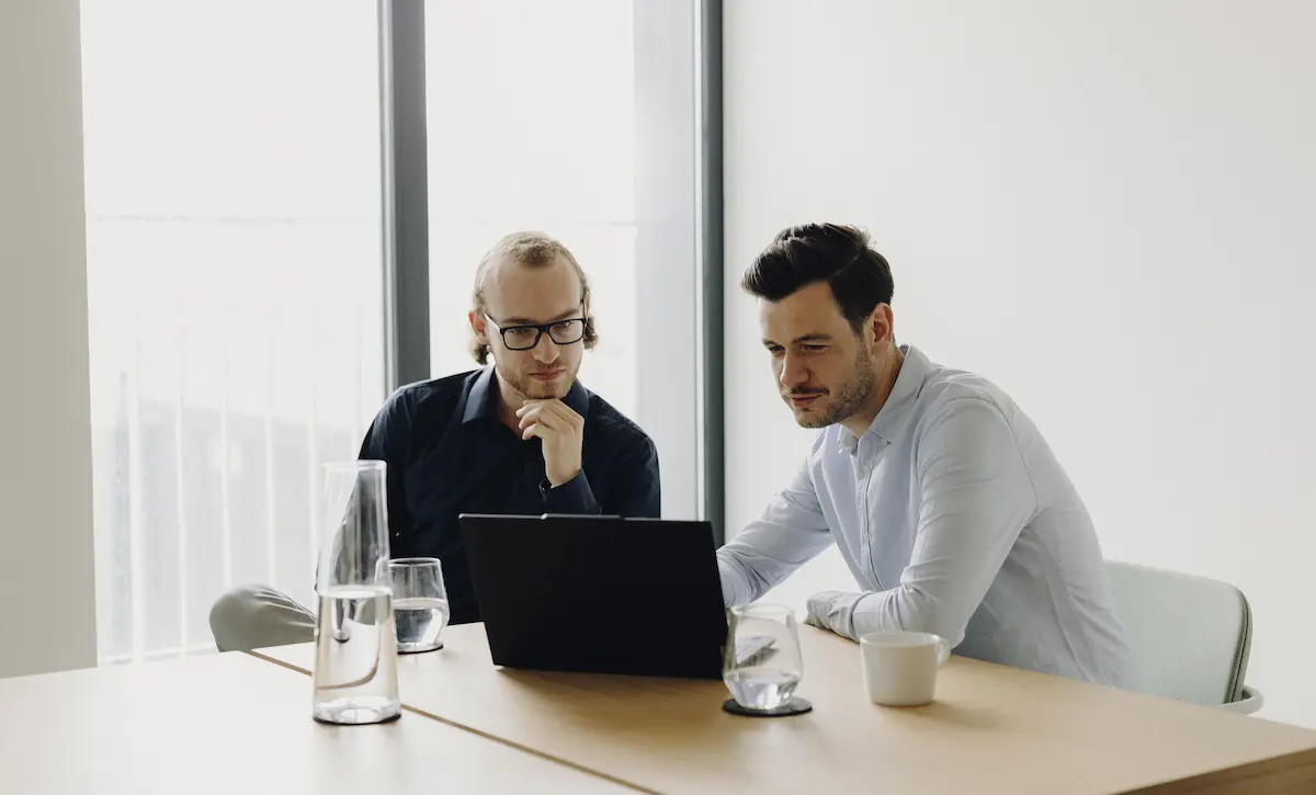 Zwei Kollegen, die an einem Tisch sitzen und gemeinsam auf den Laptop schauen