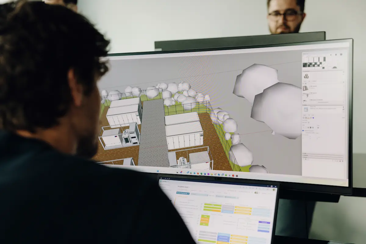 A person views a battery storage design on a computer monitor, with another person standing in the background.