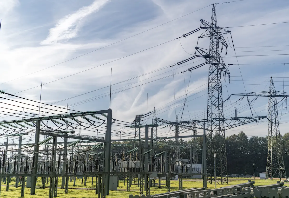 Electrical substation with towers and power lines against a partly cloudy sky.