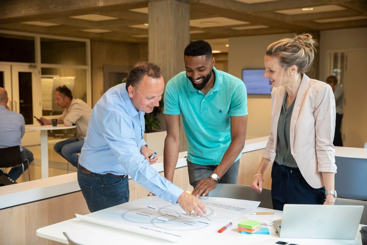 Three colleagues happily collaborate on a project, reviewing a diagram on a table in a modern office setting.