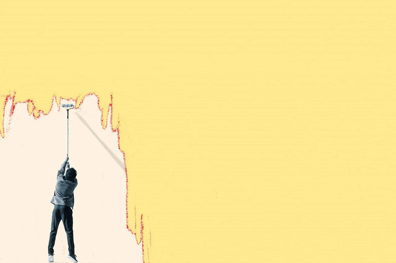 Person painting a large wall with a roller, covering vibrant colors with pale yellow.