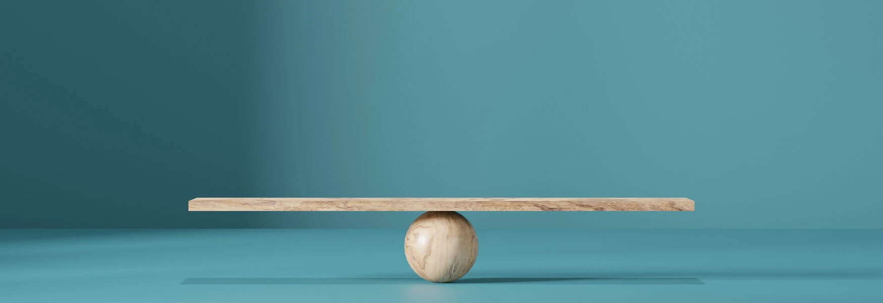 Wooden plank balanced on a round wooden sphere against a teal background.