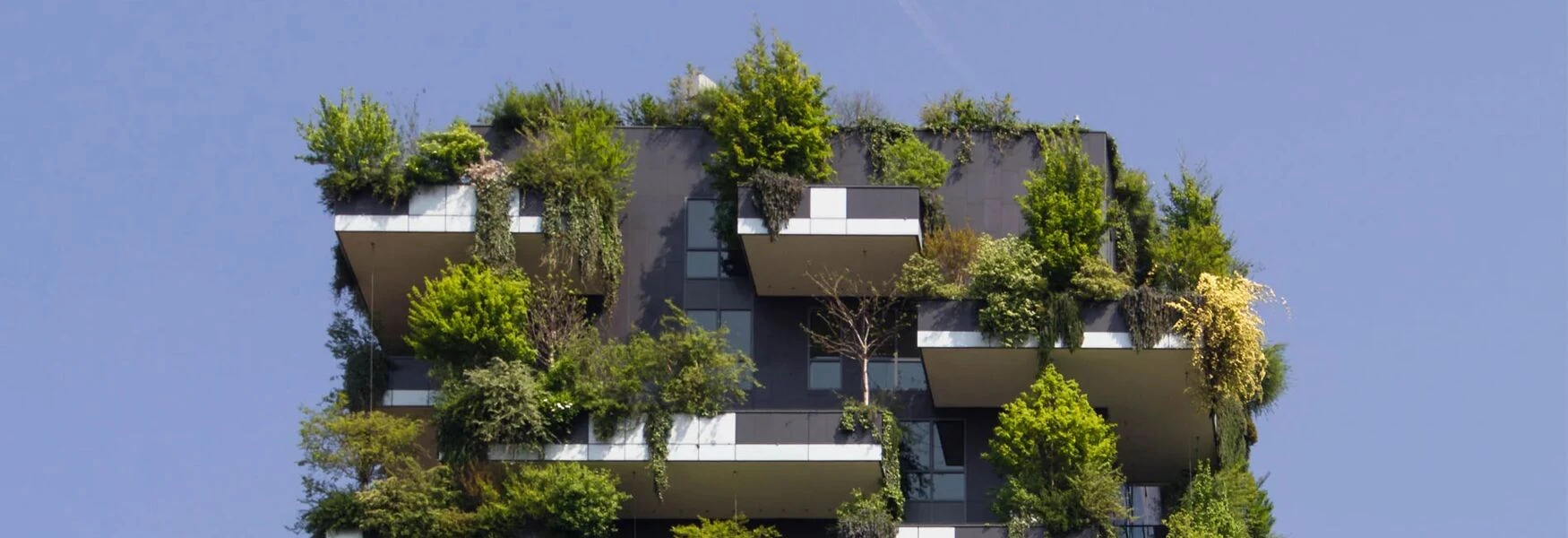 Modern building with lush greenery on balconies against a clear blue sky.