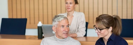 Three people engaged in a discussion in a classroom setting, with one person in the background looking attentive.