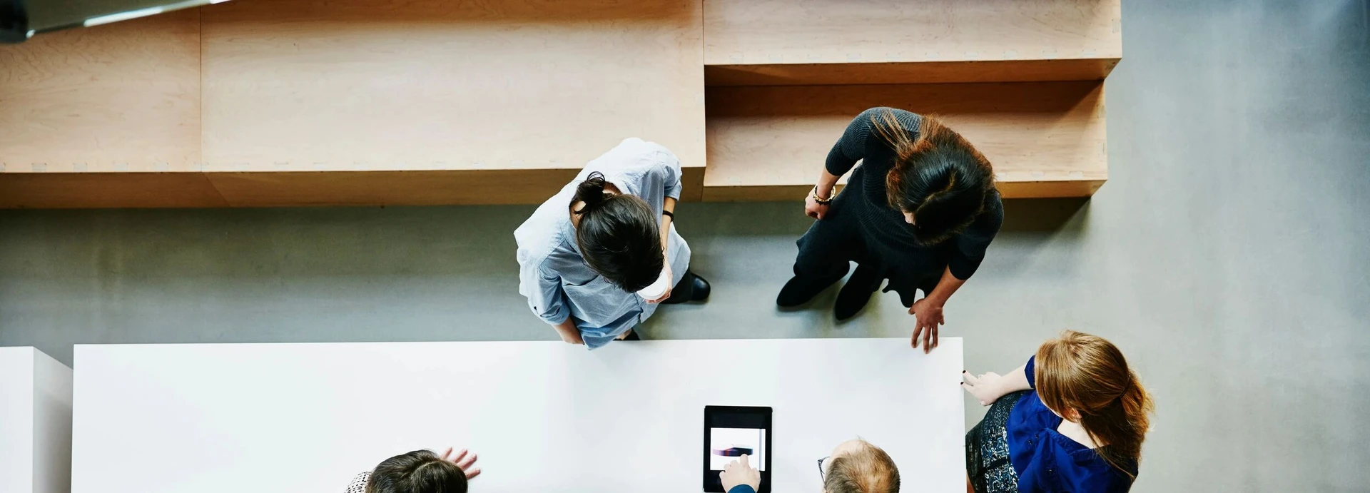 People gathered around a table, viewed from above, discussing and interacting with a tablet device.