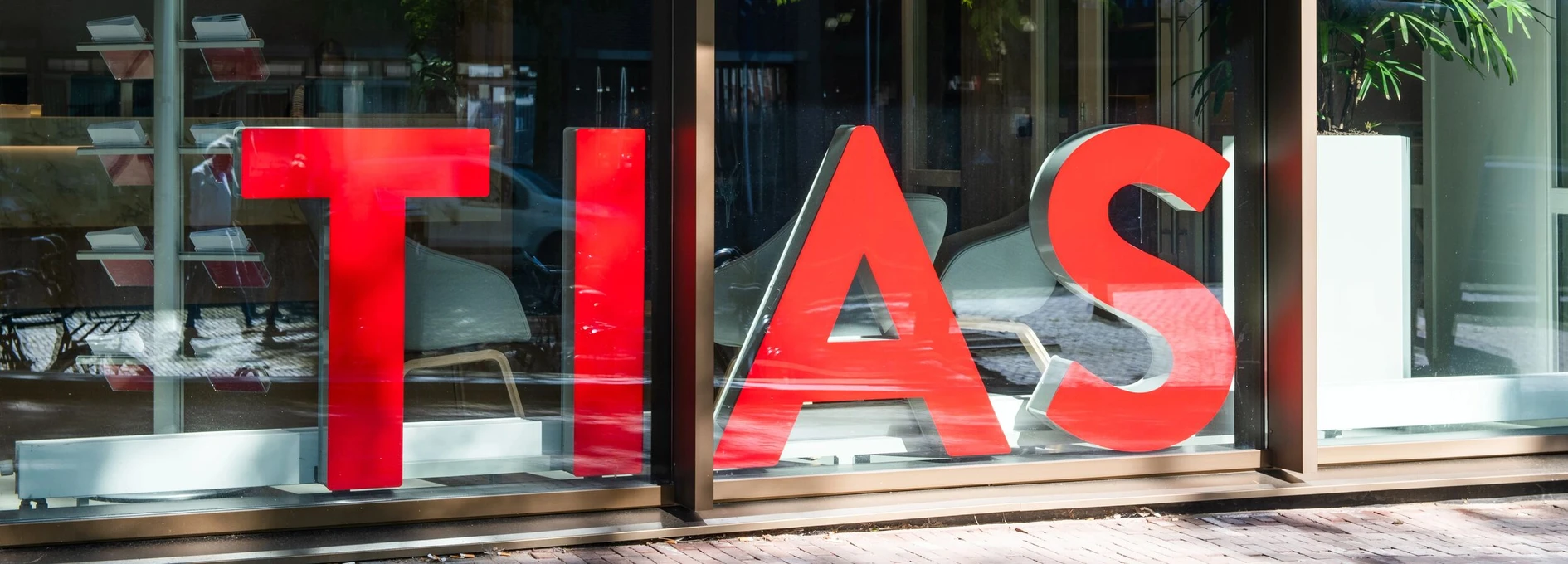 Large red "TIAS" sign displayed in a window, with reflections and greenery visible.