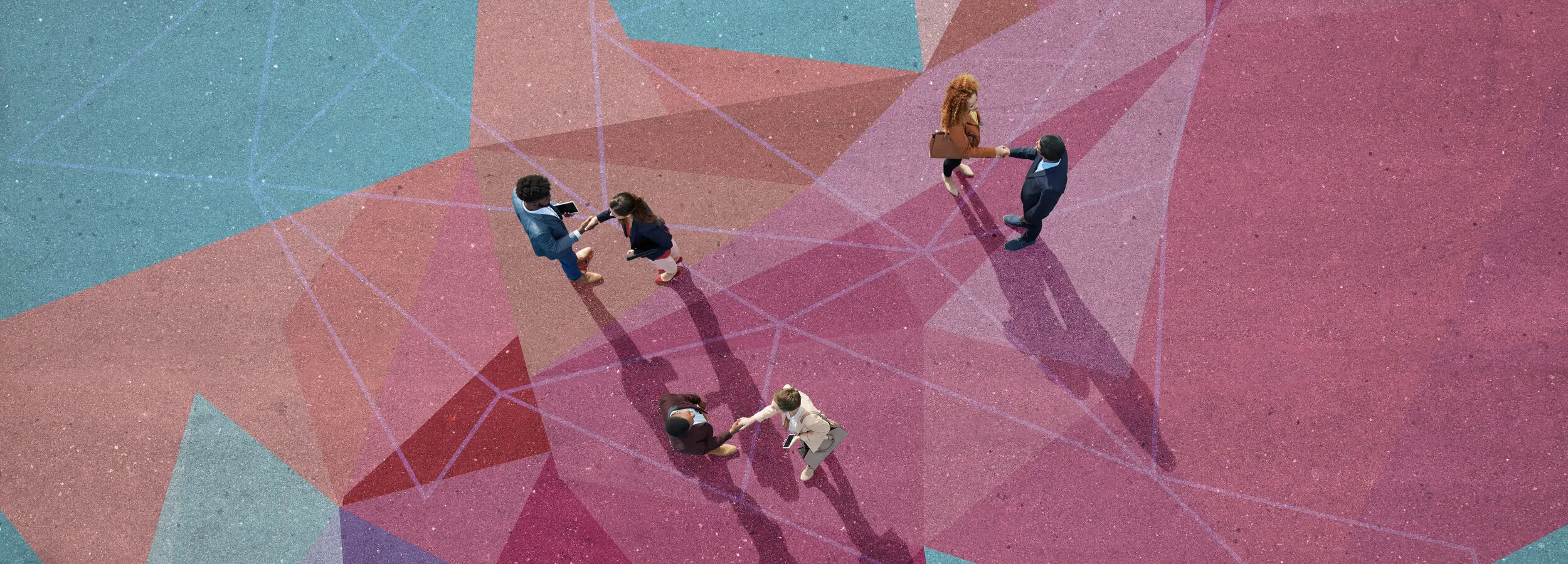 Aerial view of people walking on a colorful, geometric-patterned surface, casting long shadows in various directions.