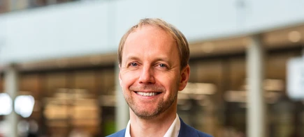 Smiling person in a professional setting with a blurred indoor background.