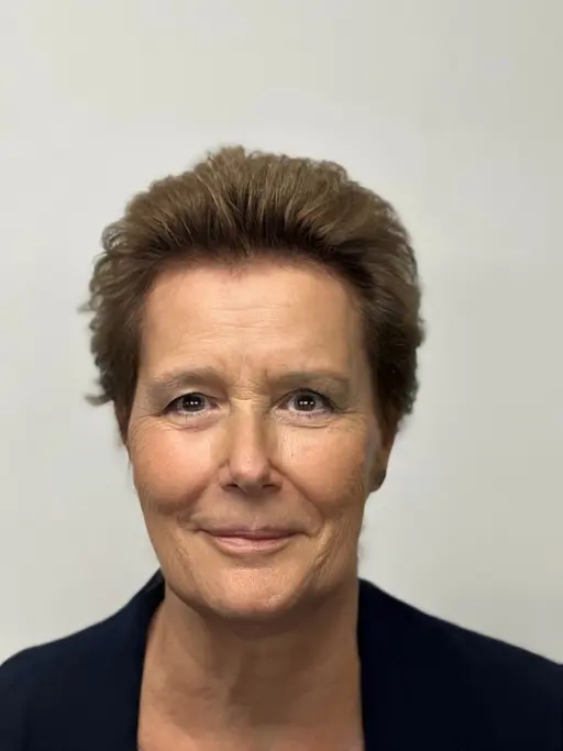 Portrait of a person with short brown hair and a neutral expression, wearing a dark blazer, against a plain background.