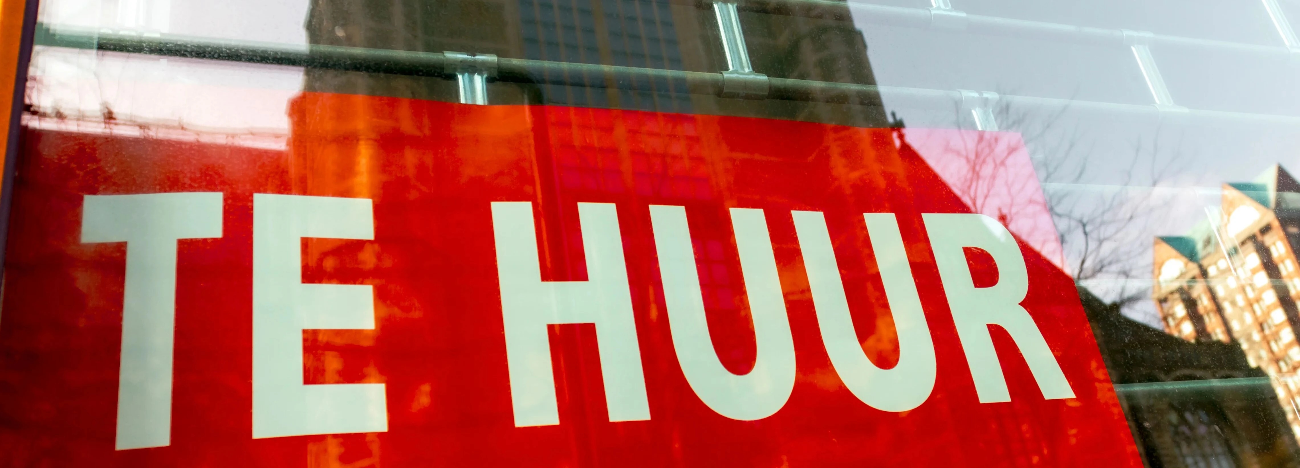 Red "Te Huur" sign in a window, indicating a space available for rent, with reflections of buildings in the glass.