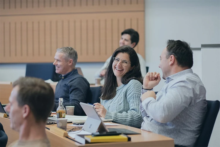 Professionals engaged in a lively discussion during a business school class, smiling and interacting attentively.