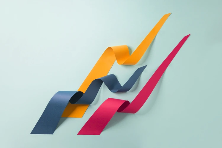 Colorful paper ribbons in blue, yellow, and red arranged in upward, wavy lines on a light teal background.