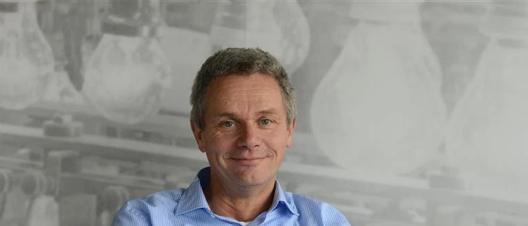 Smiling man in a blue shirt with a blurred background of light bulbs.