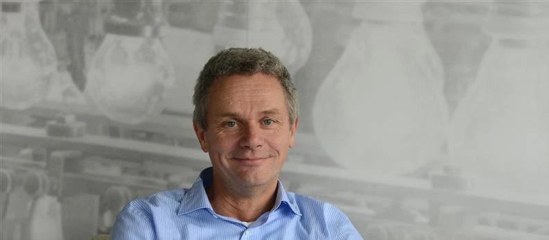 Smiling man in blue shirt with blurred background of large light bulbs.