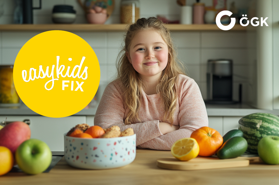 Ein junges Mädchen sitzt lächelnd an einem Küchentisch, auf dem Obst und Gemüse liegen