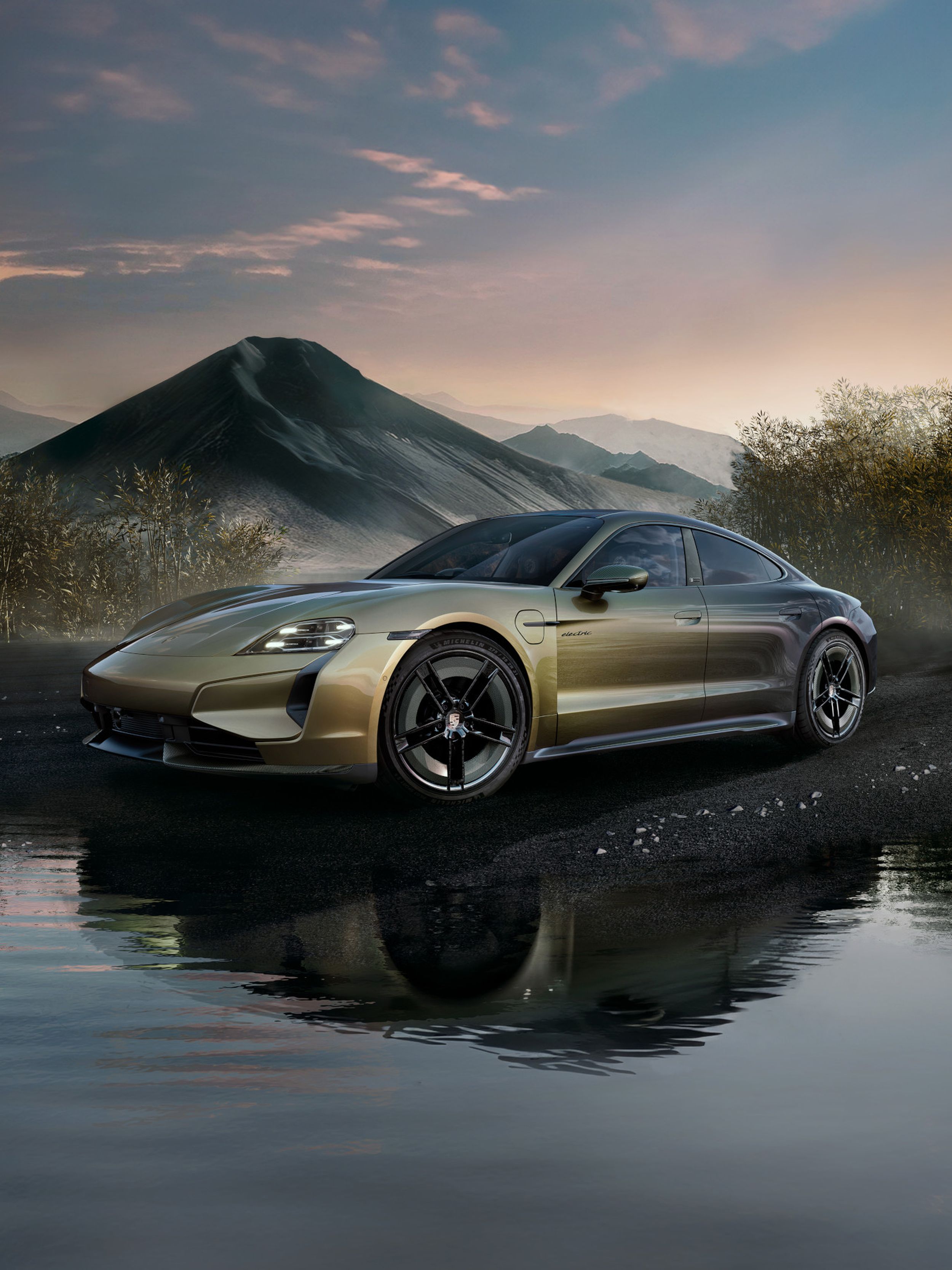 Goldmetallic Porsche Taycan auf nassem Kies positioniert mit dramatischer vulkanischer Berglandschaft und Morgennebel im Hintergrund.