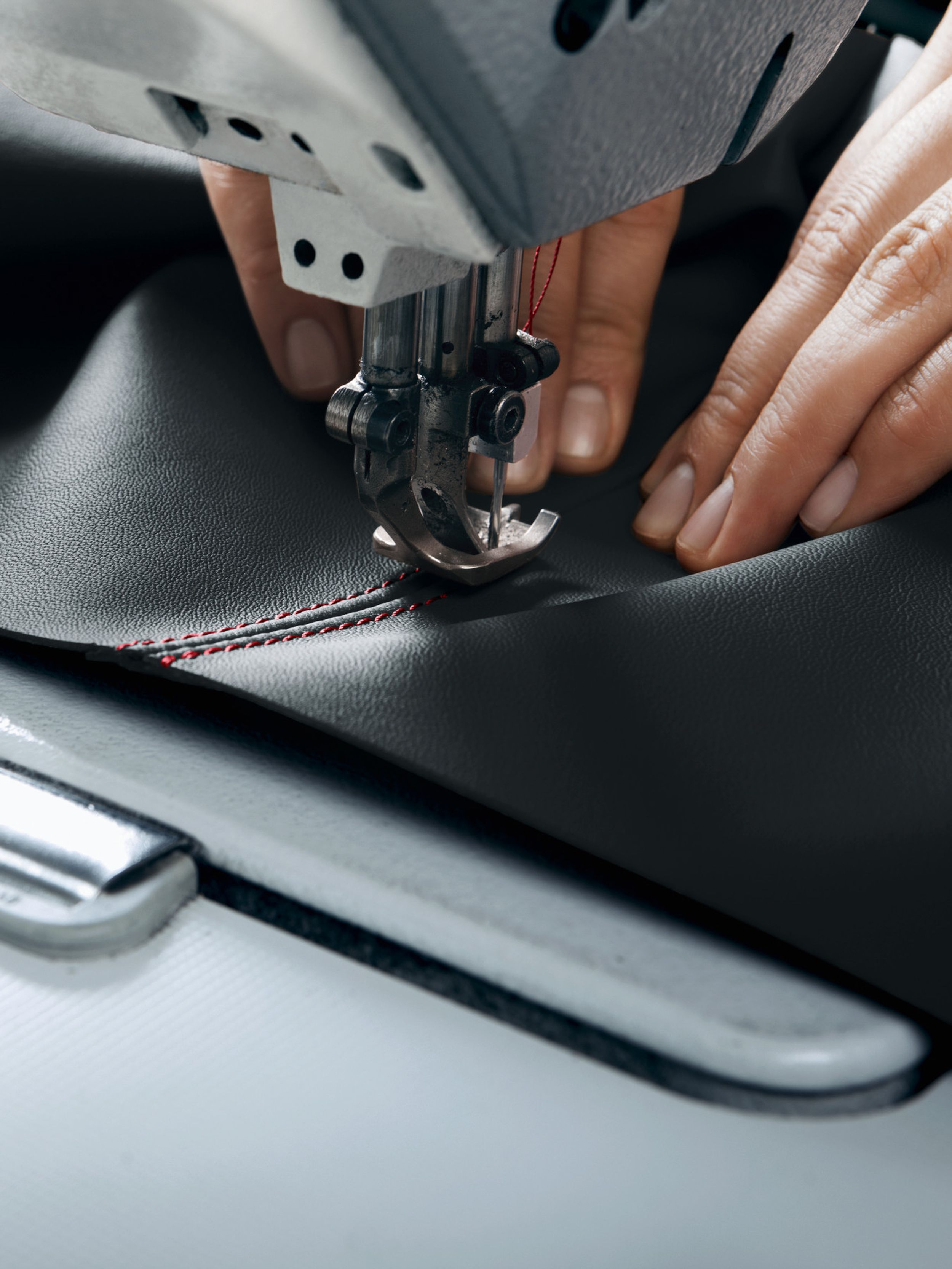 Handwerker vernäht schwarzes Leder mit rotem Kontrastgarn an einer Industrienähmaschine und zeigt die handwerkliche Qualität der Porsche-Innenausstattung.
