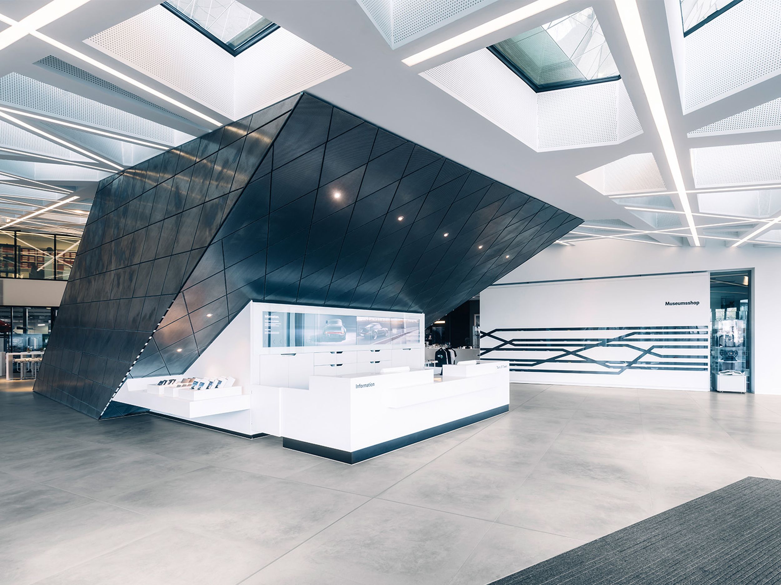 Offener Eingangsbereich des Porsche Museums mit markanter schwarzer, kantiger Architekturstruktur und weißem Informationscounter