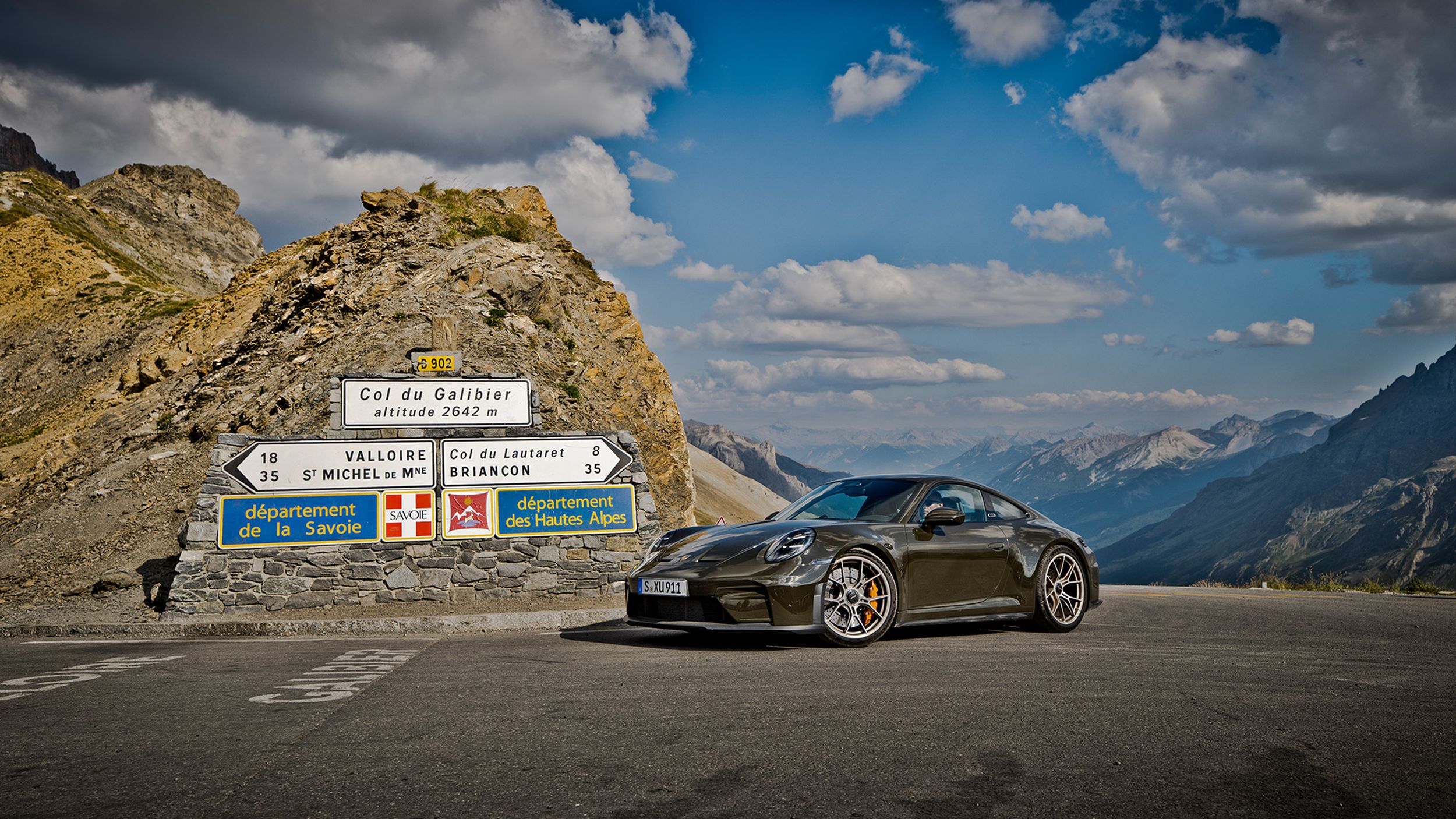Porsche 911 GT3 Bergsport am Col du Galibier auf 2642 m mit Wegweisern und Alpenpanorama unter blauem Himmel.