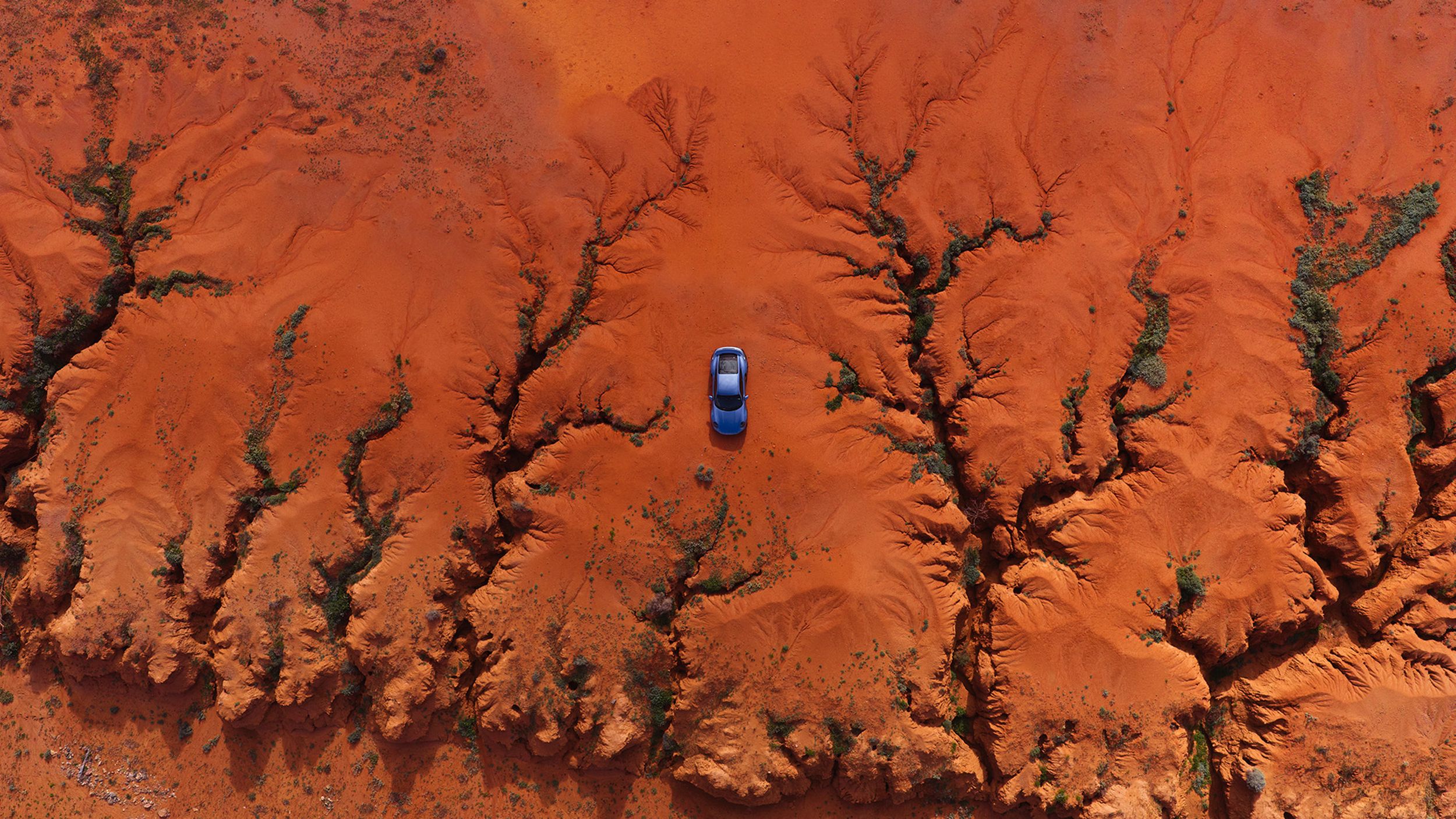 Aerial view of a blue Porsche car in the outback.