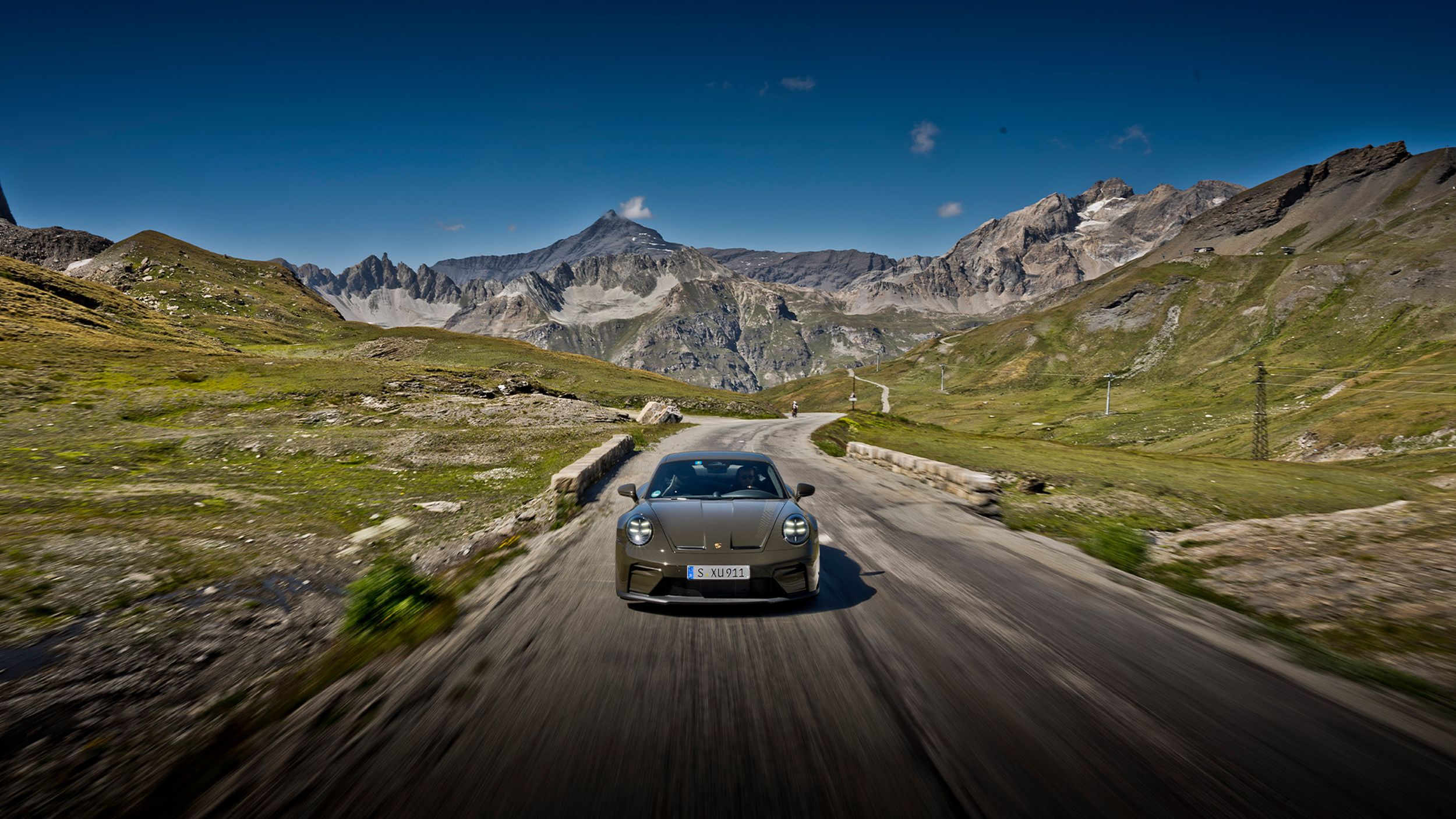 Porsche 911 GT3 Bergsport von vorne auf einer Alpenpassstrasse mit Hochalpenwiesen und Bergpanorama.
