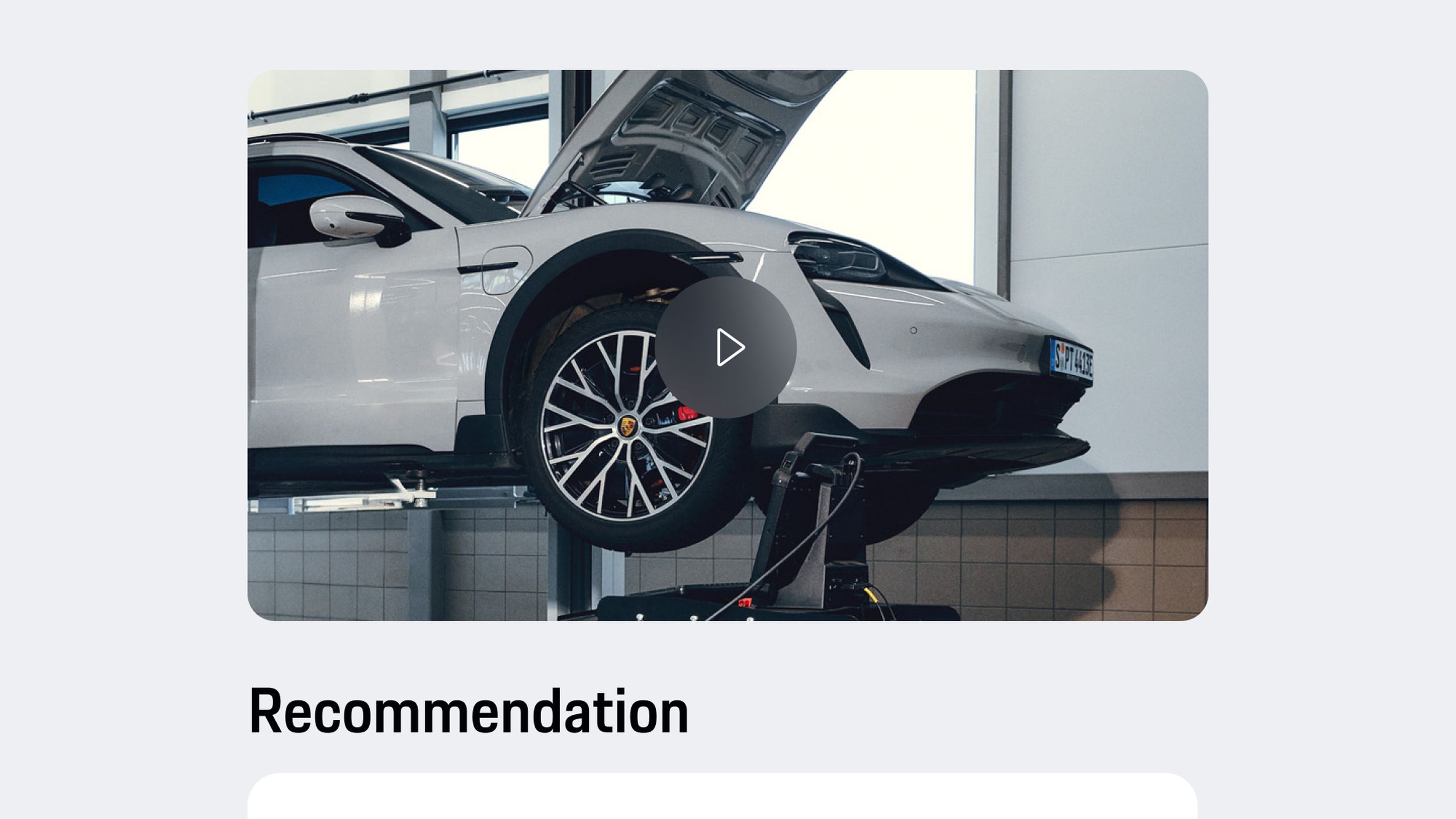 App view showing light gray Porsche on lift with open hood, video play button and recommendation text displayed below.