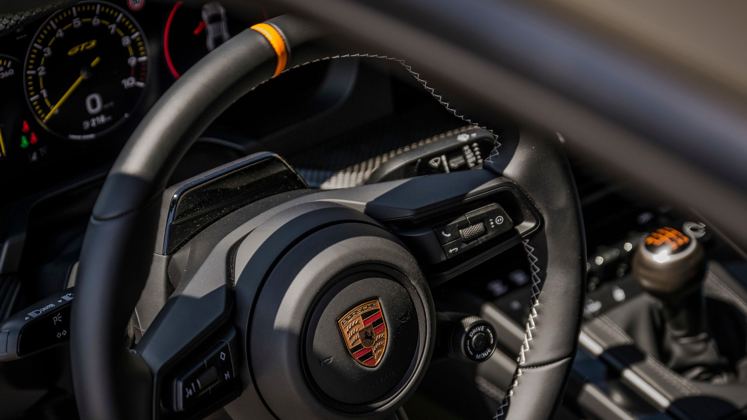 Nahaufnahme des Porsche 911 GT3 Bergsport Lenkrads mit Porsche Wappen und gelber Lenkradmarkierung.