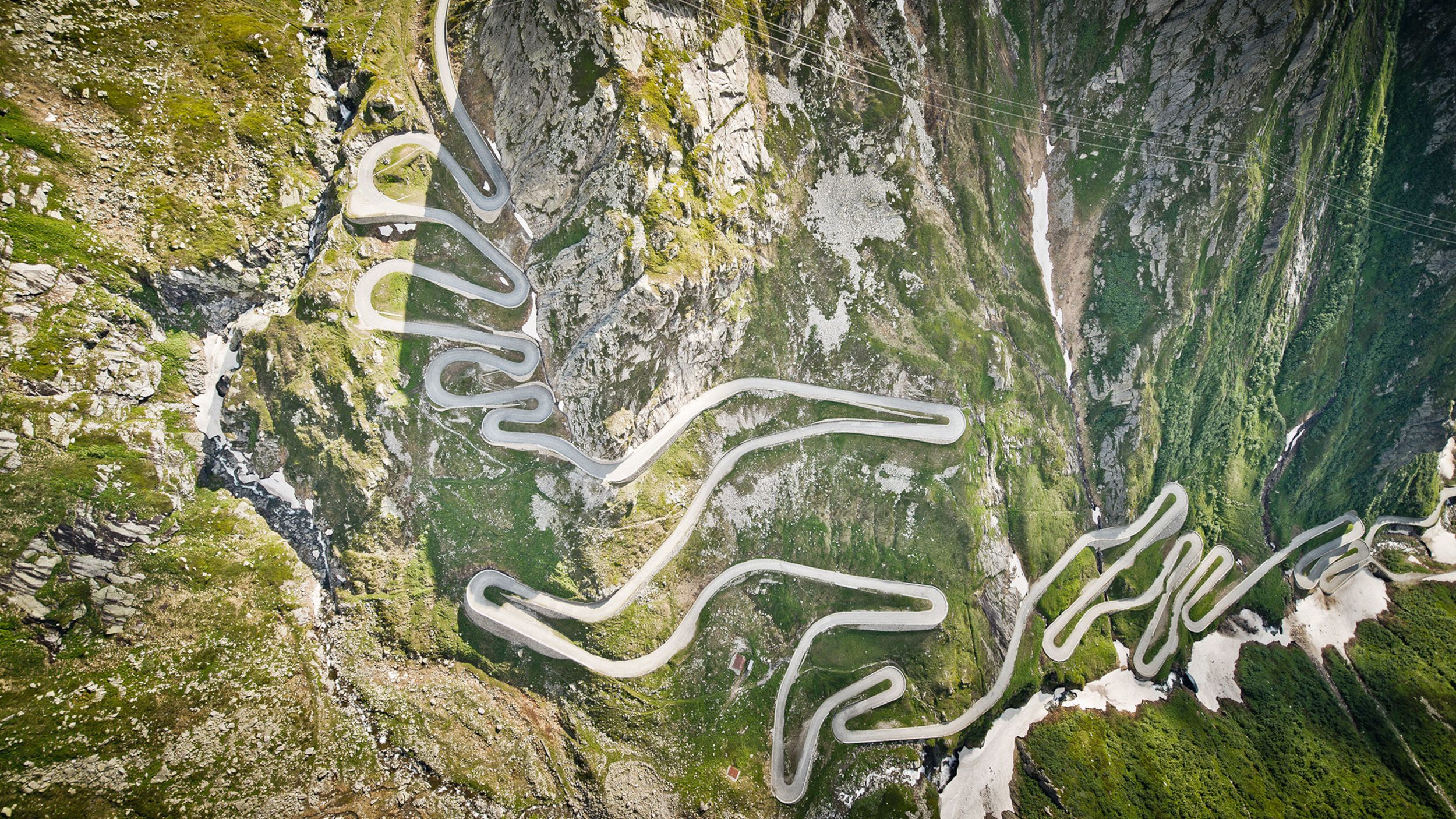 Luftaufnahme einer kurvigen Bergpass-Strasse durch eine Alpenlandschaft.