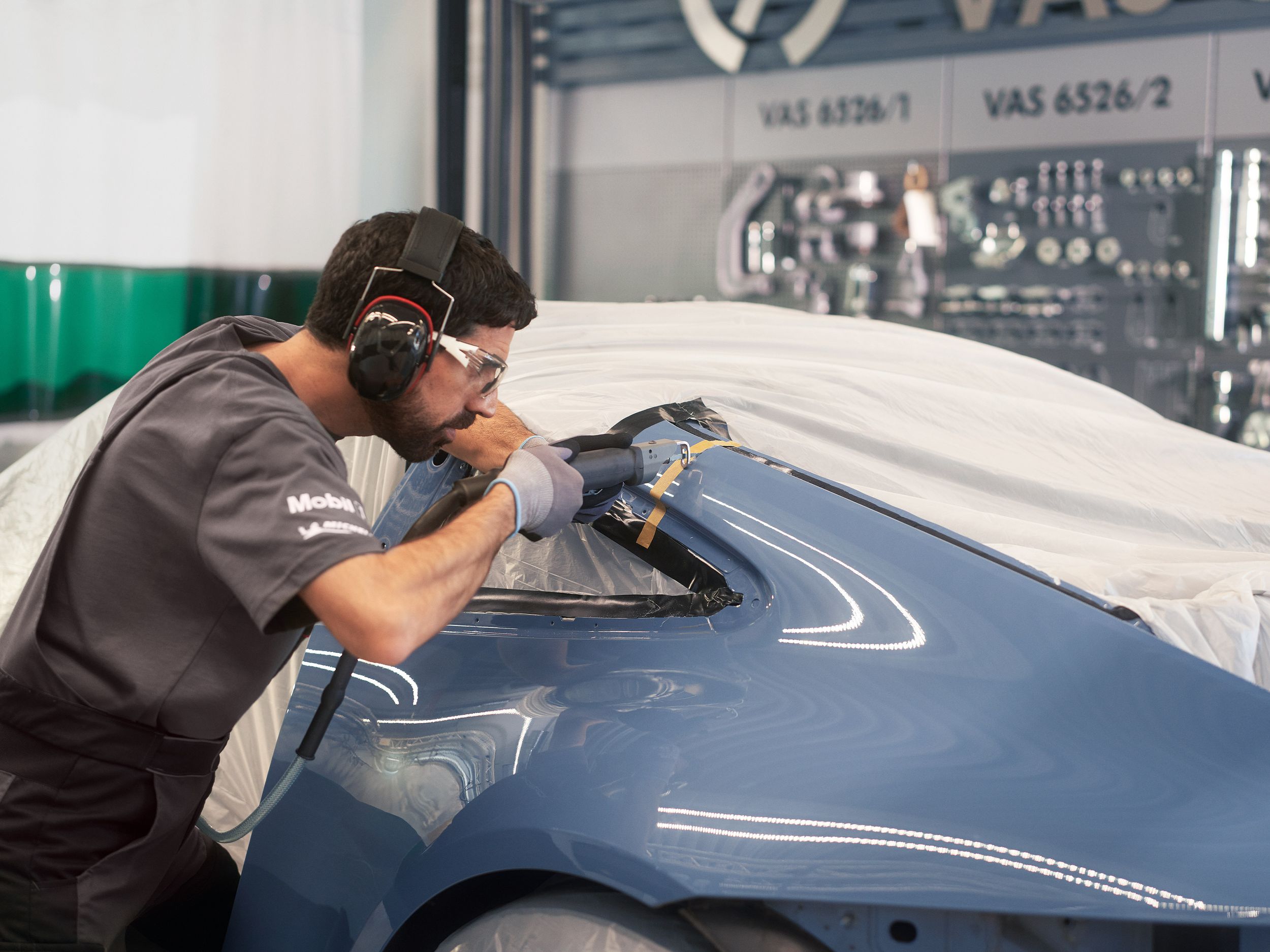Porsche mechanic with safety glasses using a body saw on a blue taped-up Porsche body panel in a Porsche Service Centre.