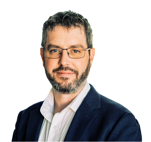 Man with glasses and a beard wearing a white shirt and dark blazer, smiling slightly against a plain background.