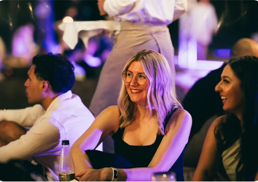 People sitting and smiling in a dimly lit, lively setting with purple lighting.