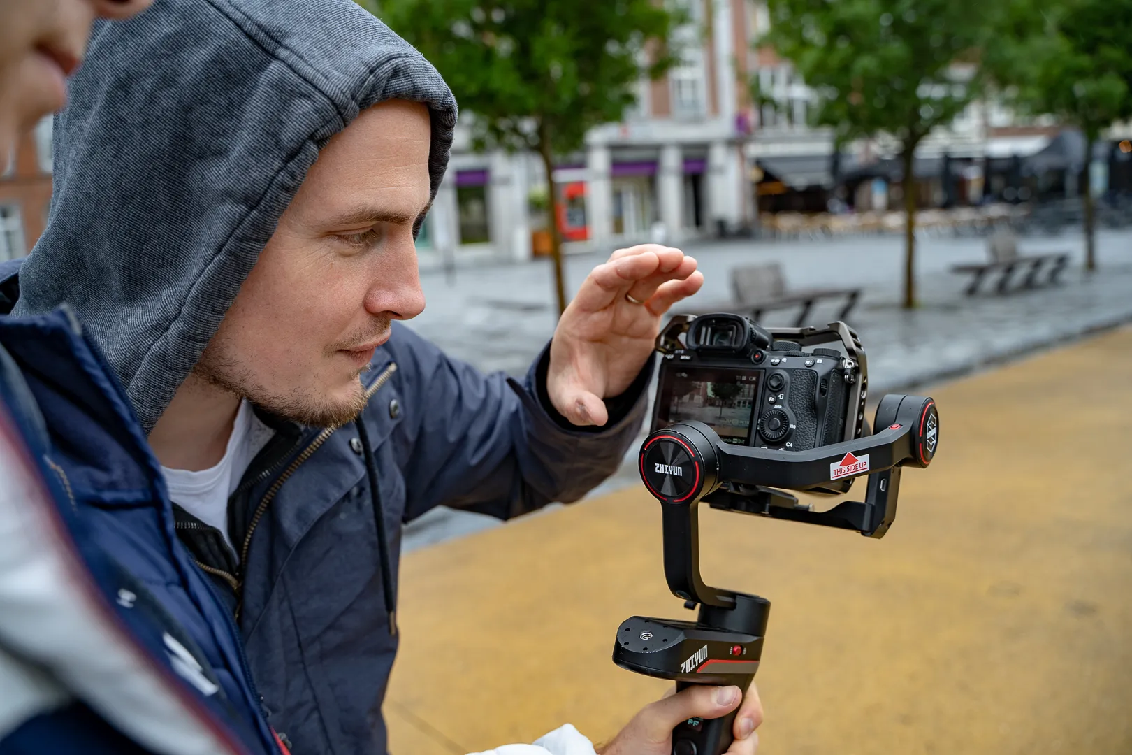 un homme en capuche est vu de profil, à côté d'un appareil photo