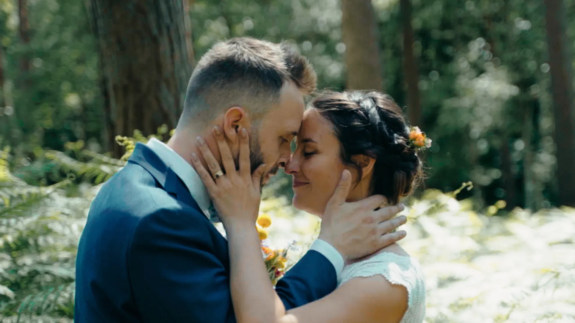 un couple de jeunes mariés se regardent, leurs fronts et nez se touchent, elle a les mains sur les joues de son mari et il a sa main posée sur le cou de sa femme