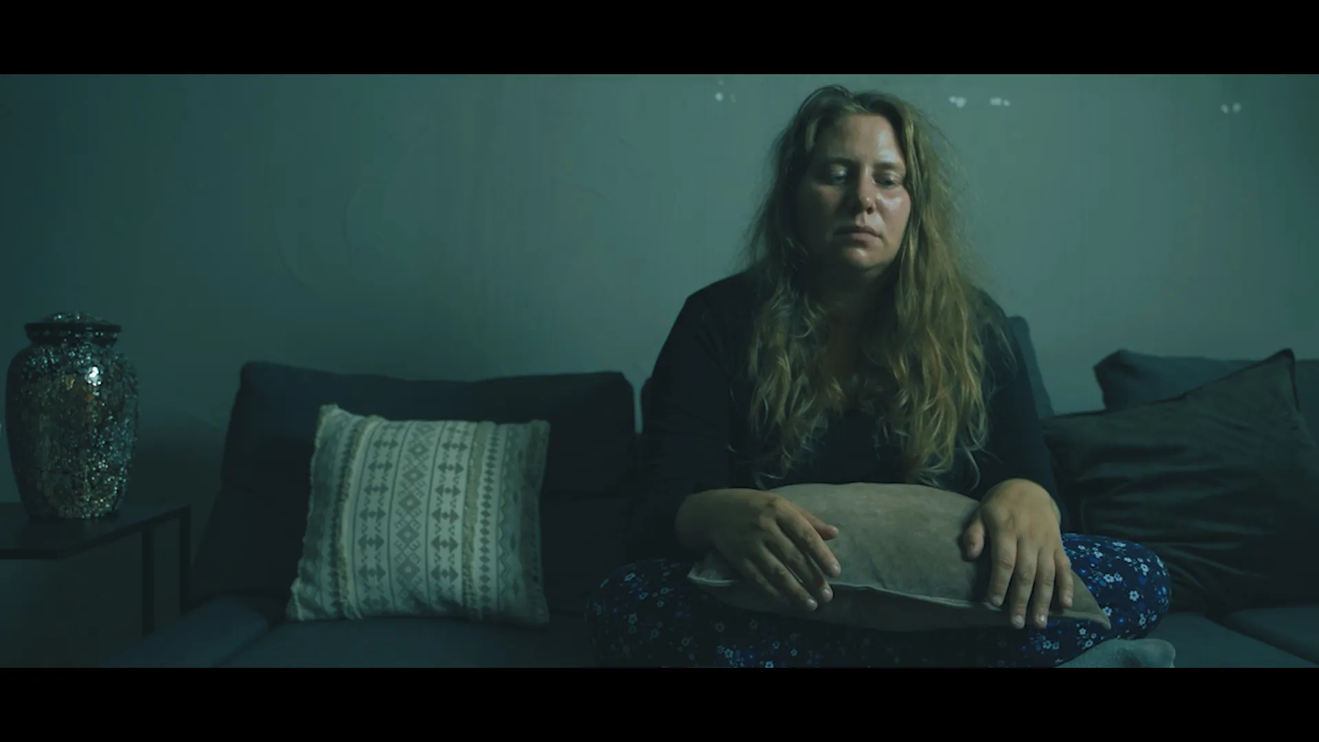 une femme aux cheveux longs est assise sur un fauteuil, elle est en larmes