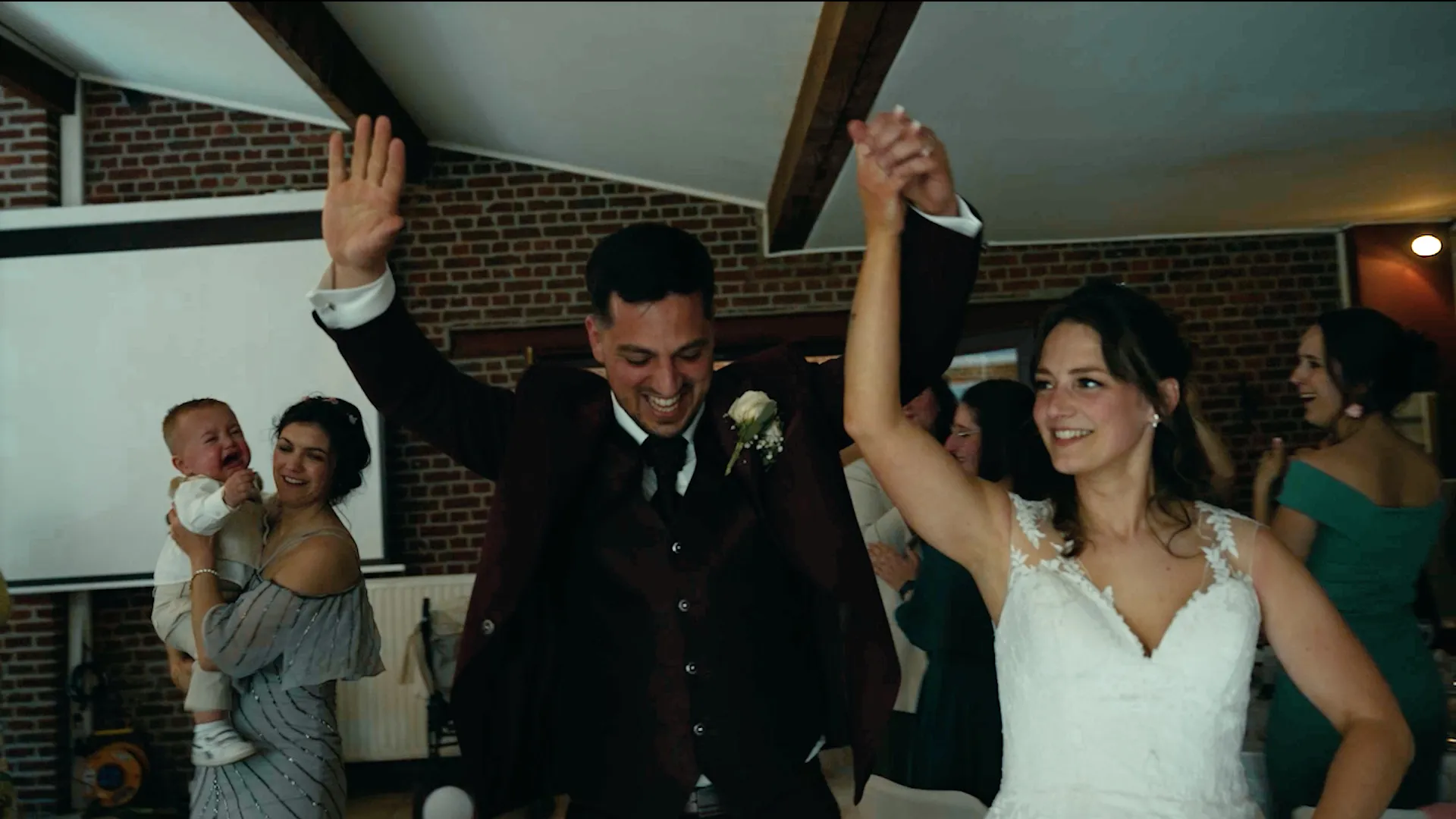 un couple de jeunes mariés danse avec les bras en l'air, un groupe de personnes qui dansent aussi est derrière eux