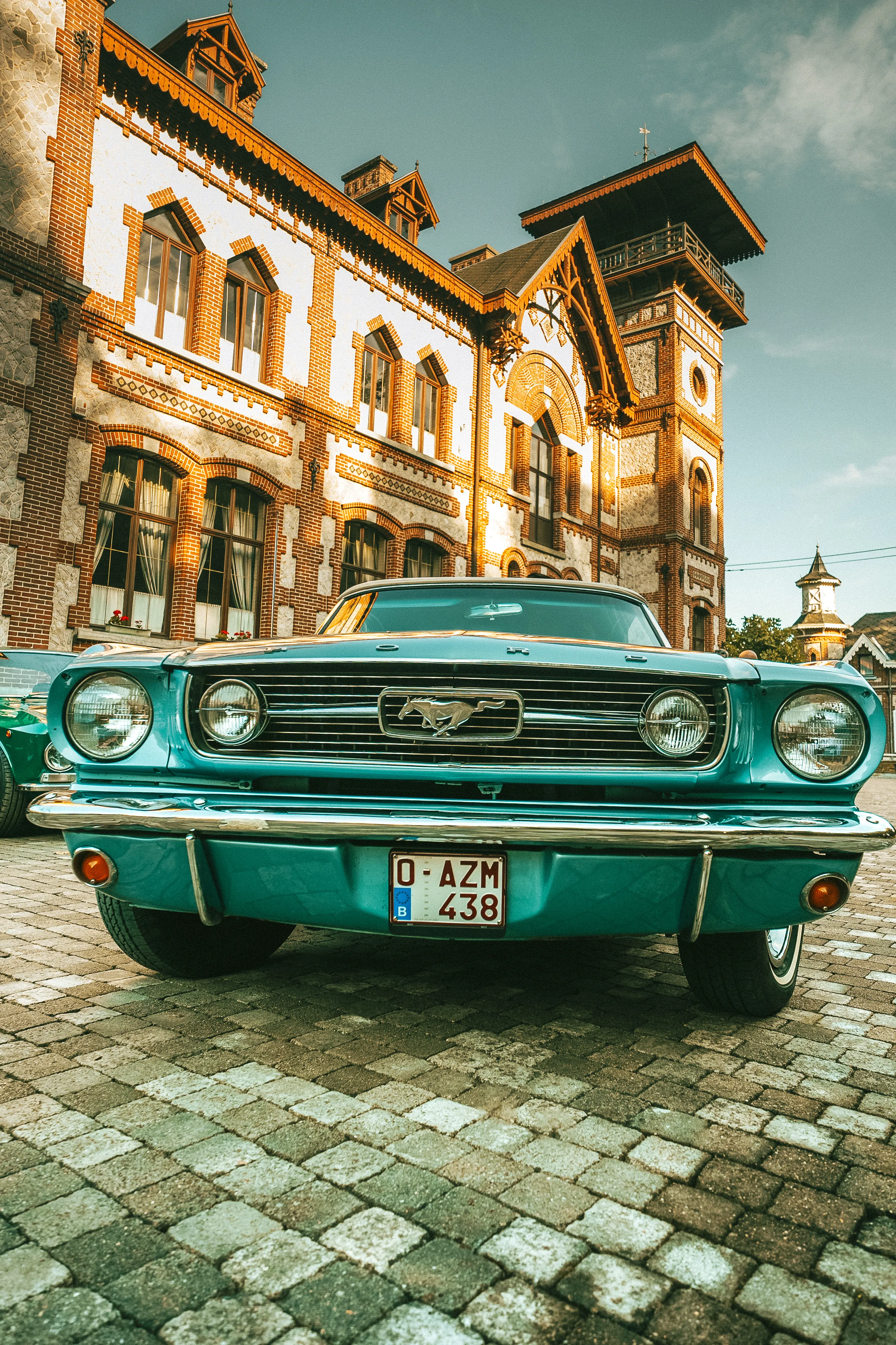 une ancienne voiture, une Mustang turquoise, est vue de face devant un beau vieux bâtiment