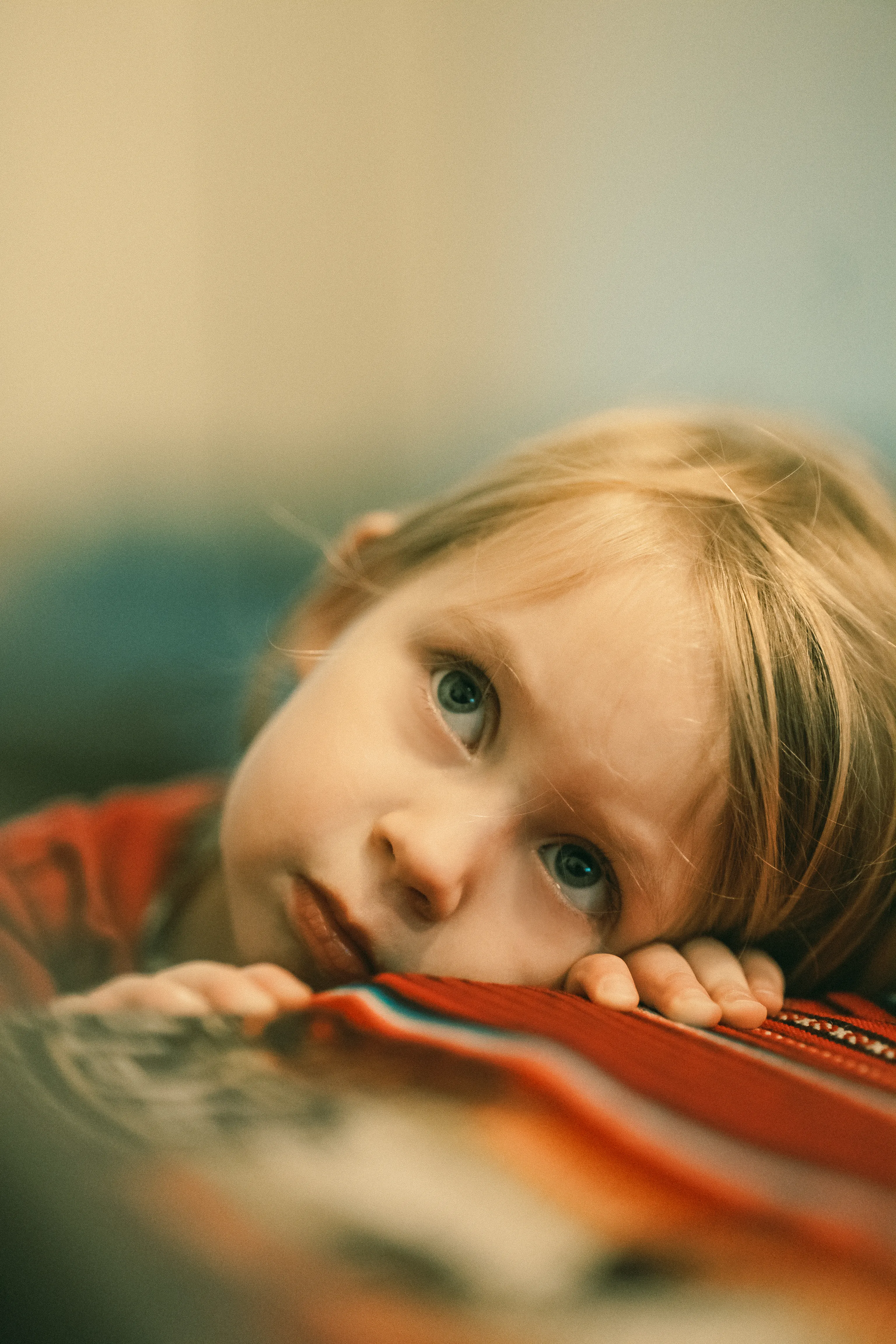 une petite fille a les deux mains posées sur une table, sa tête repose sur une main, elle regarde vers le haut