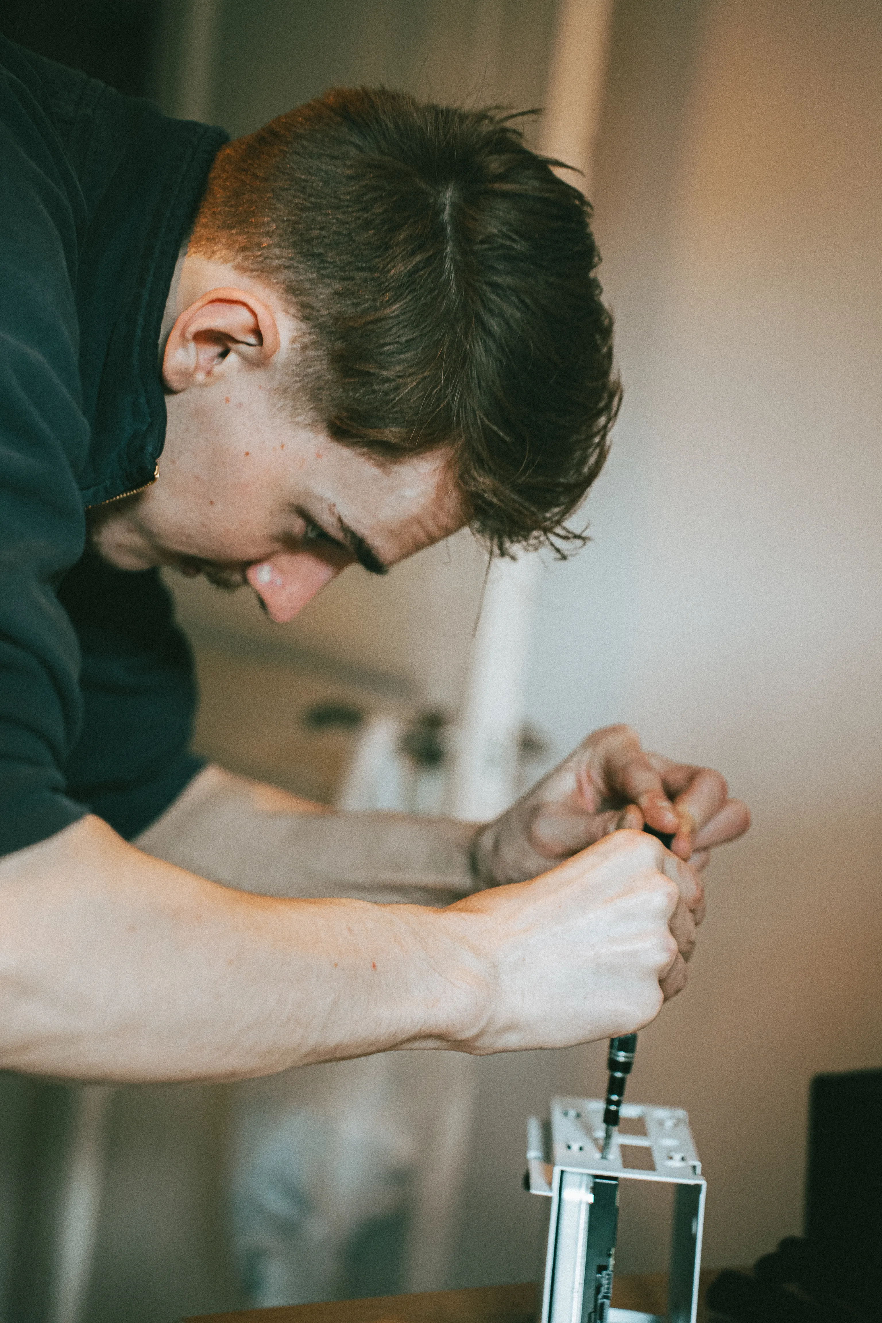 un homme est vu de profil, il a un tournevis en main et assemble une machine