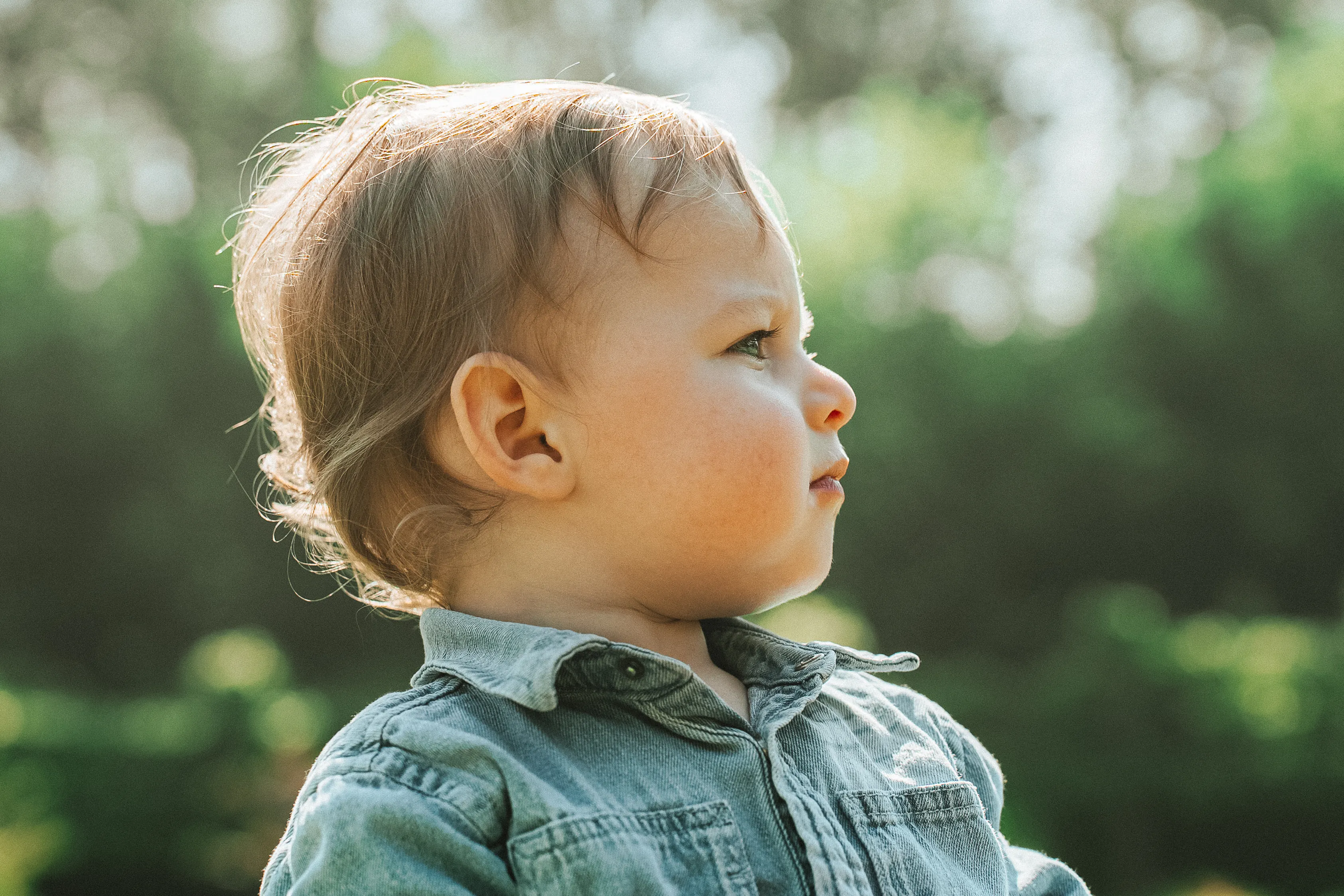 un petit garçon en chemise en jeans regarde au loin, il est de profil