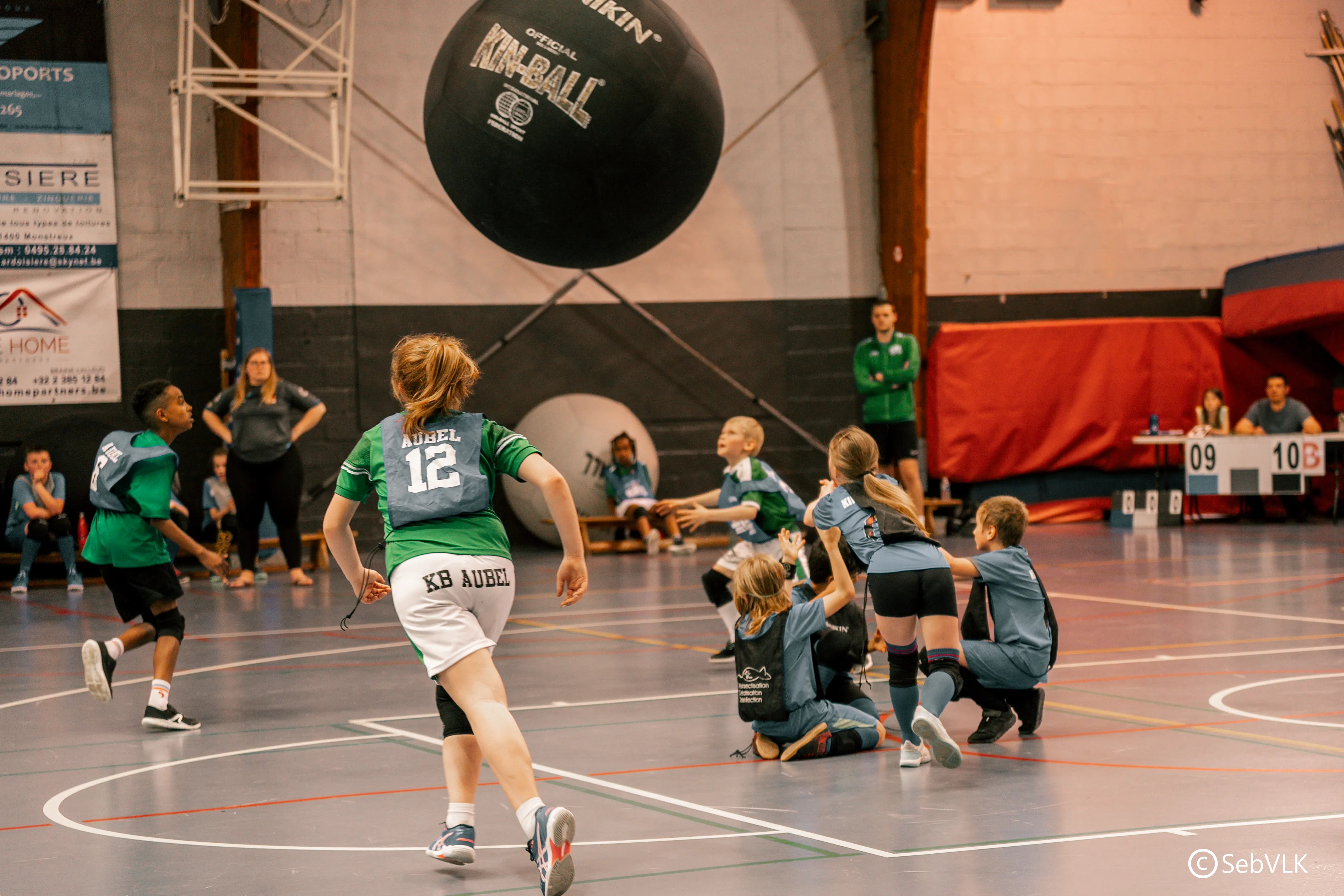 dans une salle de sport, un groupe d'enfants joue avec une grosse balle de Kin-ball - la balle est au-dessus de leurs têtes