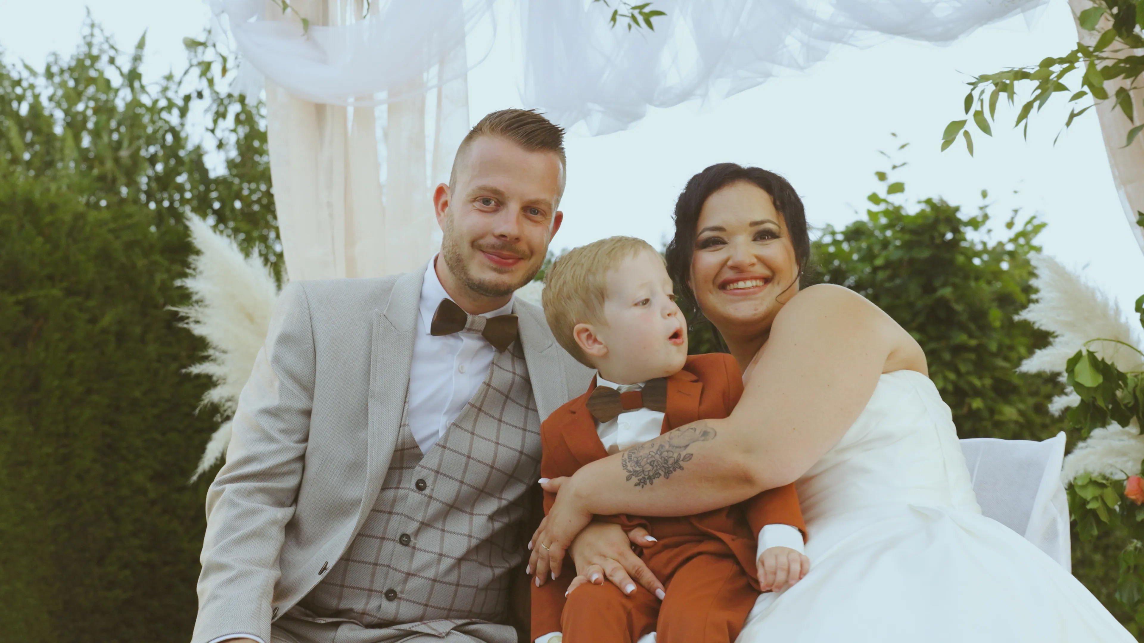 un couple de jeunes mariés est assis - la mariée a un jeune garçon en costume ochre sur les genoux