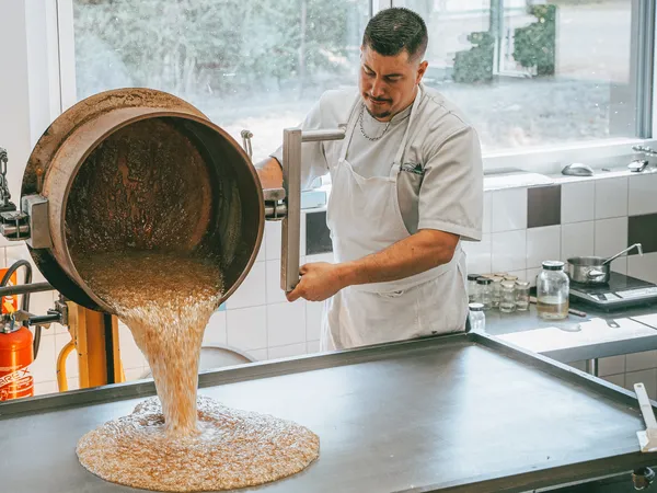 un artisan avec un tablier blanc devant une table de travail sur lequel il verse du caramel chaud