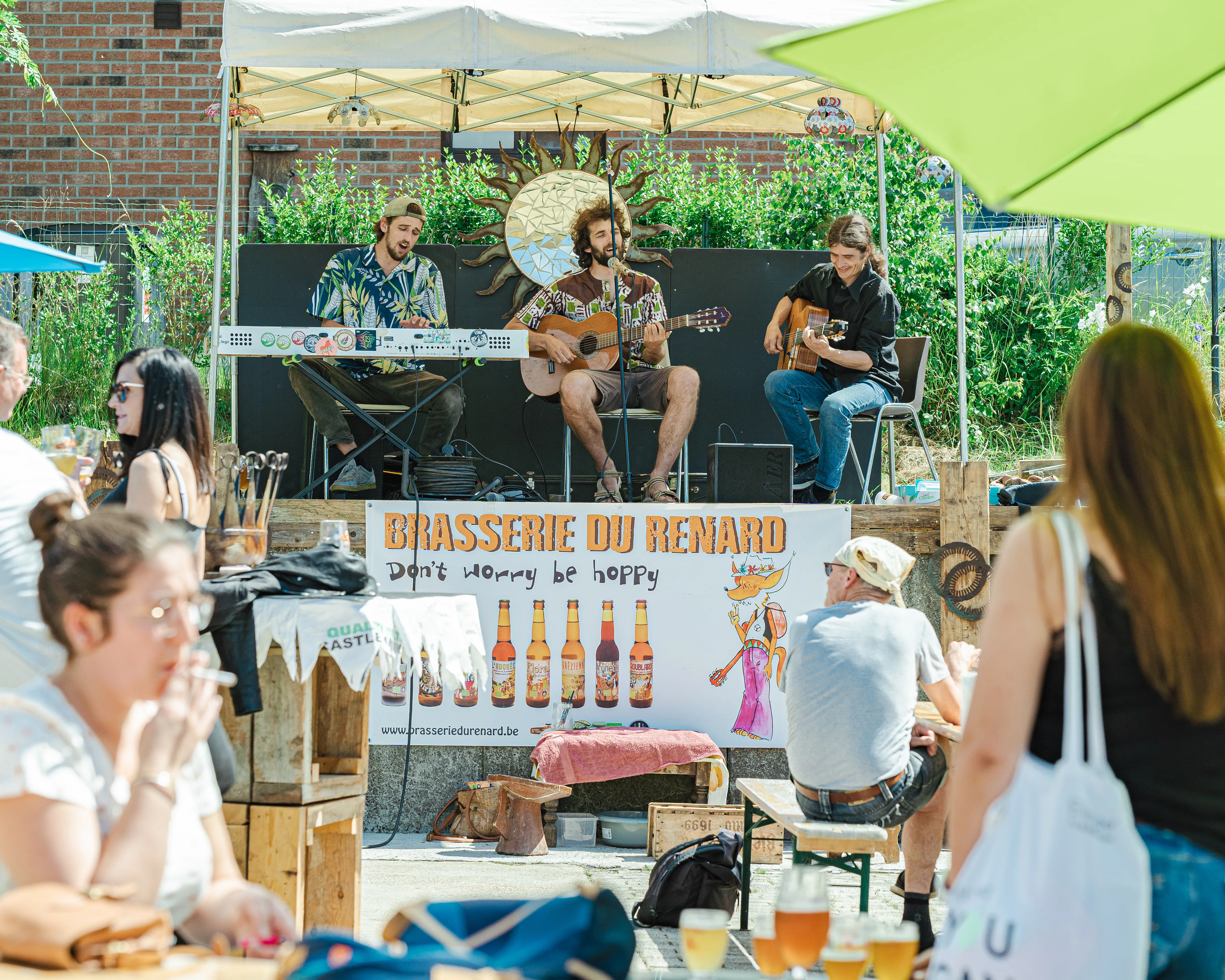 une groupe de trois musiciens joue sur un podium devant des personnes attablées à la brasserie du renard
