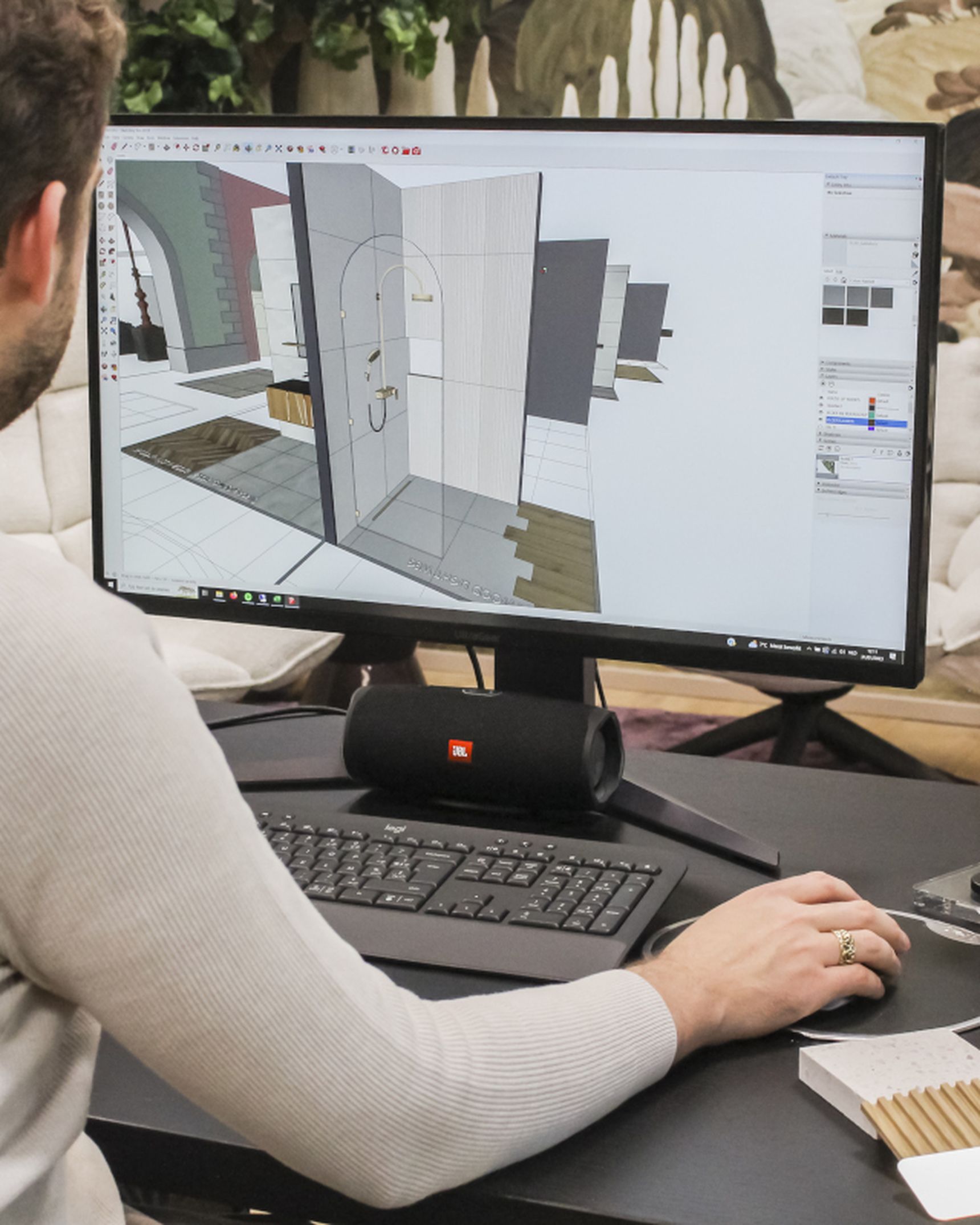 Pieter Steylaerts in witte trui aan bureau, kijkt naar 3D-badkamerontwerp op computerscherm.