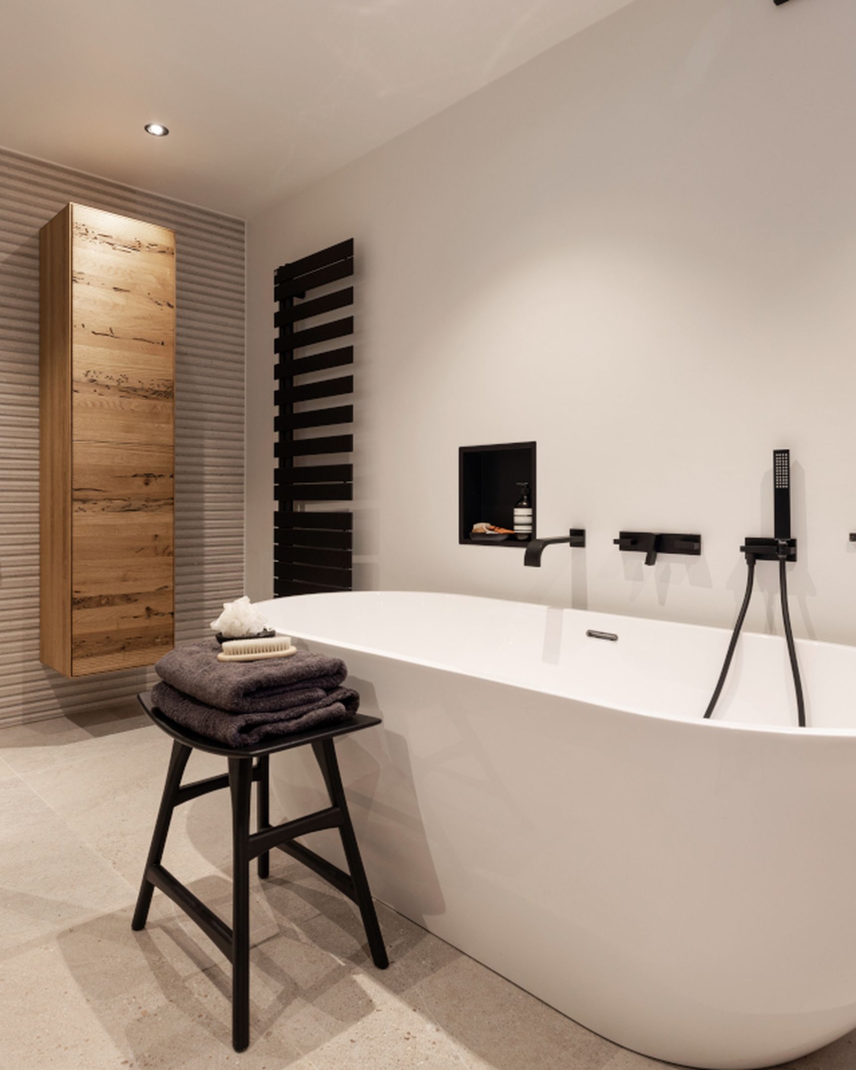 Modern bathroom with a freestanding bathtub, black fixtures, a wooden stool with towels, a glass shower partition, and a wooden cabinet.