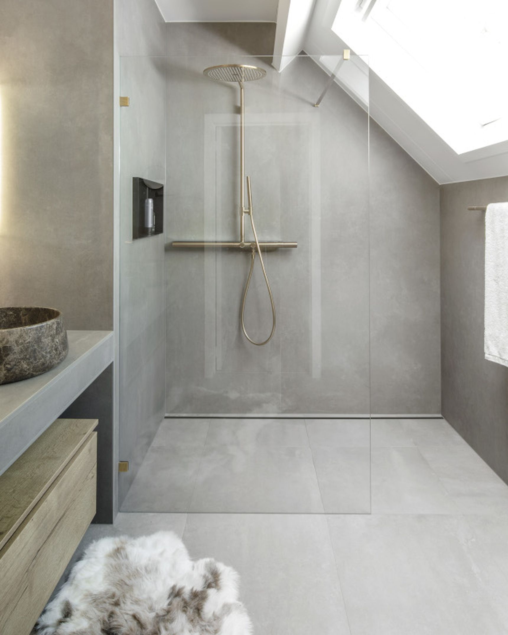 Modern bathroom with a skylight, stone sinks, a glass shower enclosure, and a towel on a rack. Neutral tones and soft lighting create a serene ambiance.
