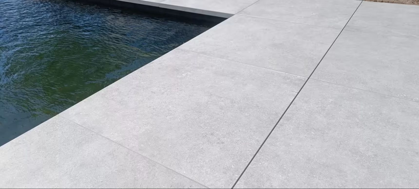 Lichtgrijze keramische terrastegels rondom een zwembad, met een strak en modern lijnenspel en onzichtbare Drainvi afwateringsgoot.