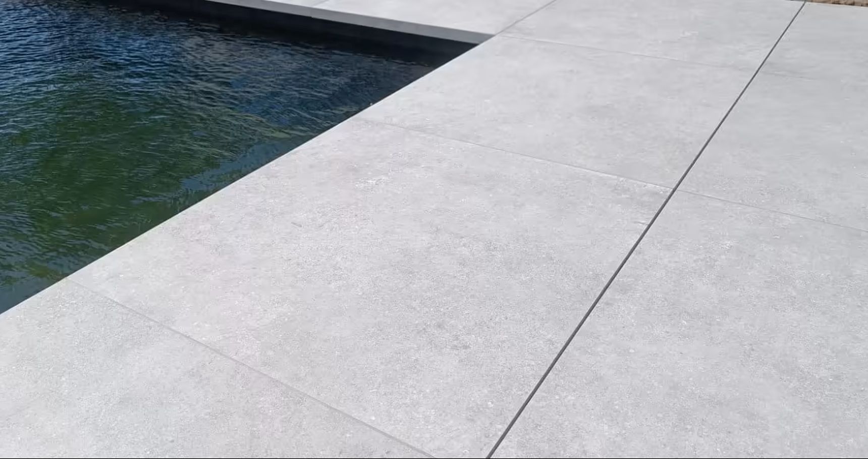 Lichtgrijze keramische terrastegels rondom een zwembad, met een strak en modern lijnenspel en onzichtbare Drainvi afwateringsgoot.