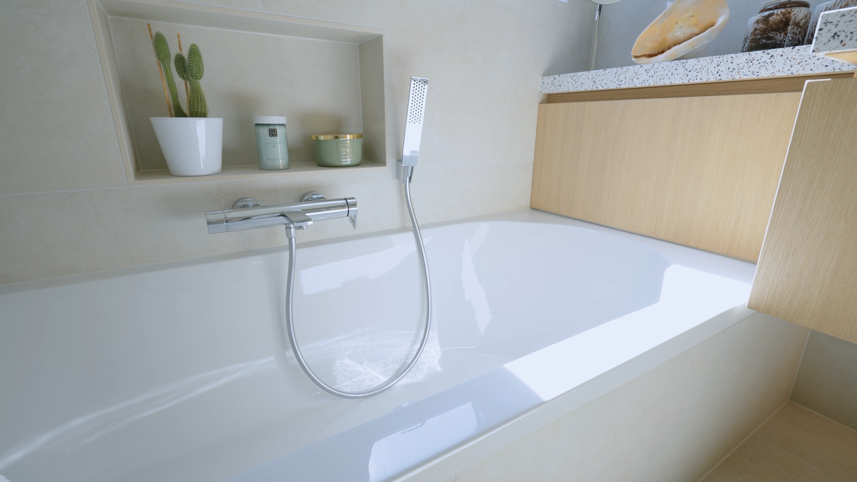 Modern bathroom with a white bathtub, built-in shelf holding a cactus and candles, and a handheld showerhead.