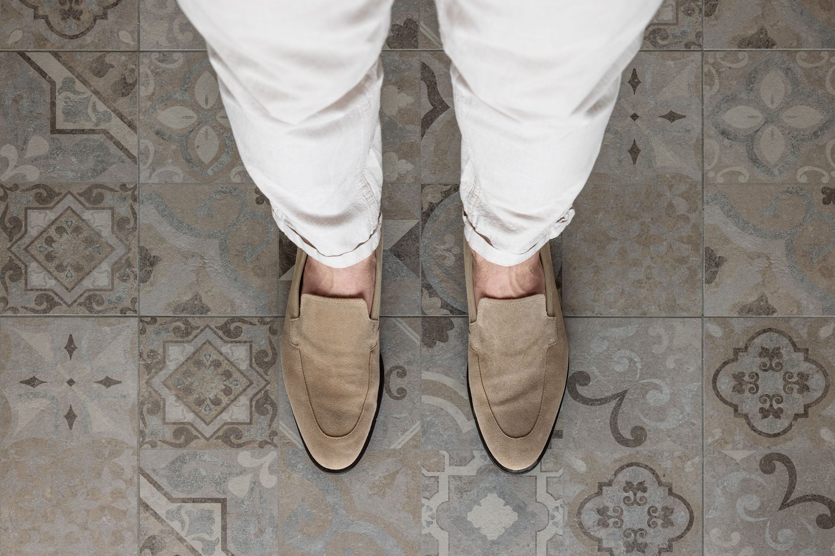 Persoon met beige loafers en witte broek staat op patroontegels met geometrische en bloemmotieven.